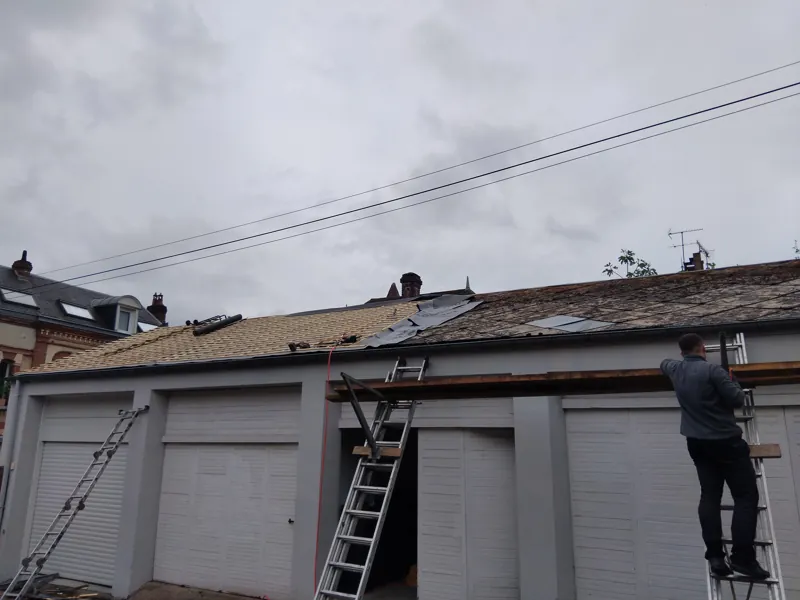 Couvreur sur échelle devant une rangée de garages