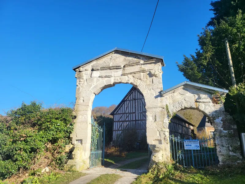 Portail ancien en pierre devant une ferme à colombages