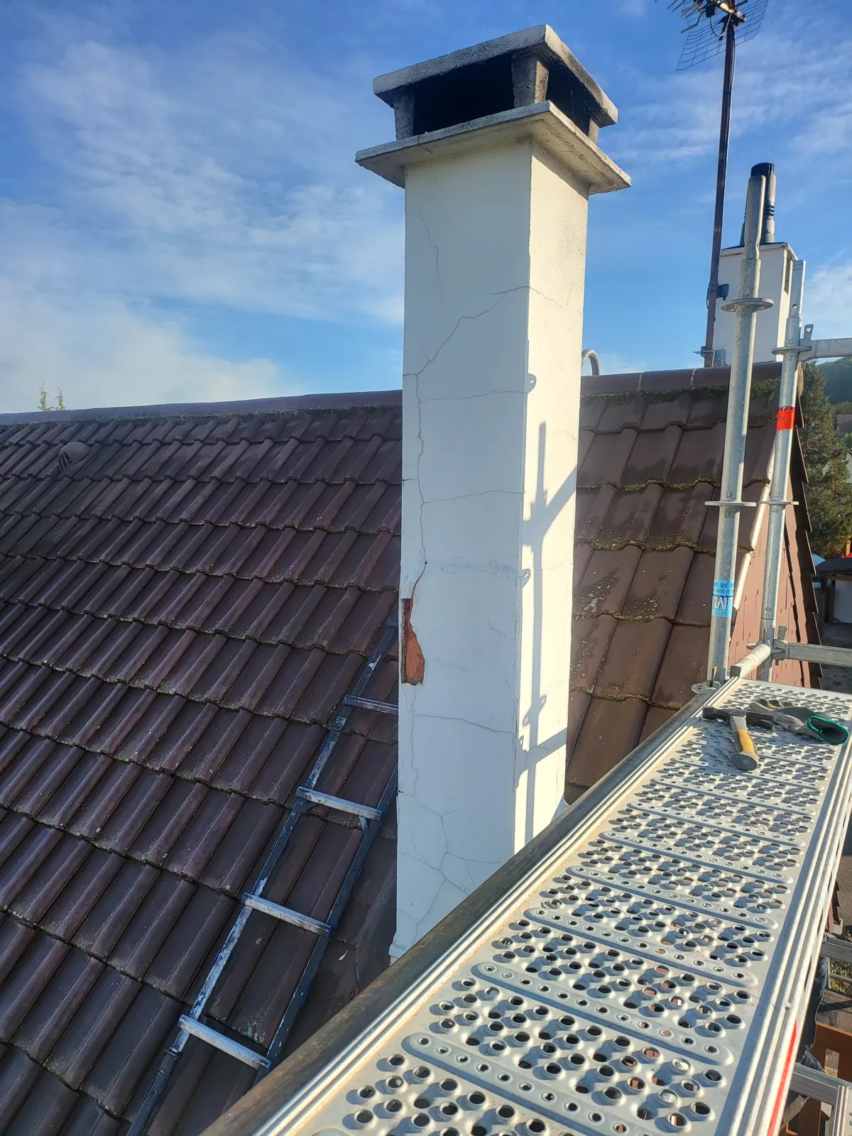 Souche de cheminée enduite sur une toiture en tuiles, vue depuis l'échafaudage