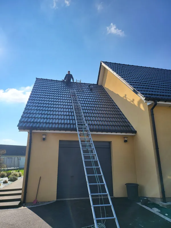 Couvreur sur une toiture en tuiles noires, échelle contre le pignon