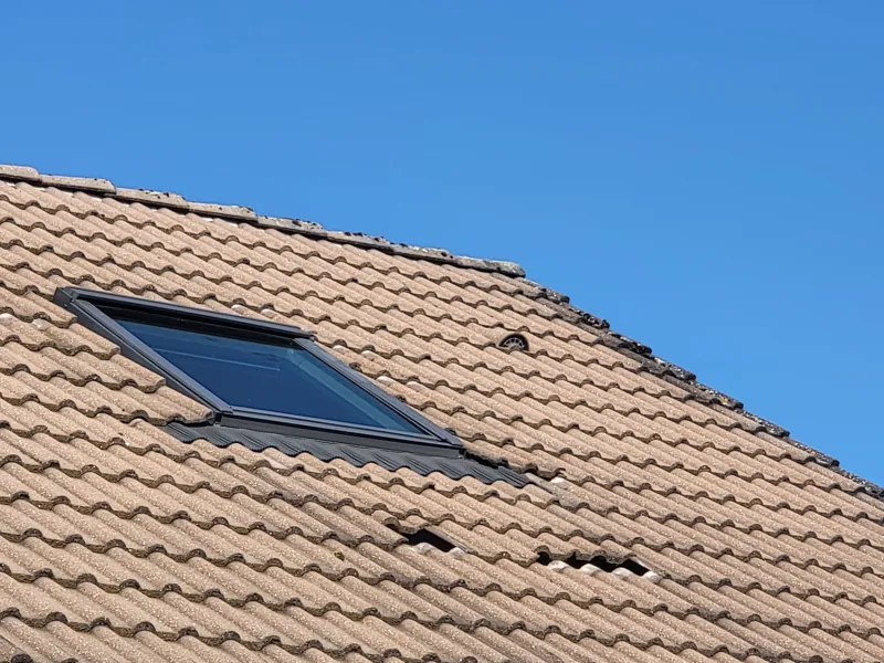 Fenêtre de toit sur une toiture en tuiles, tuiles soulevées à côté